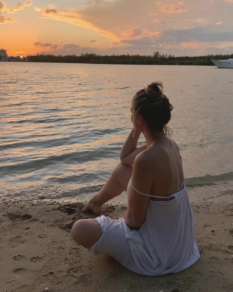 Shayna Daniel sitting by the water at sunset